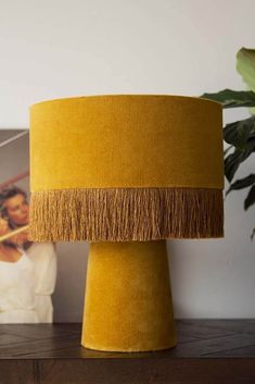 a yellow table lamp with fringe trim on the base and a woman standing behind it