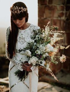 a woman wearing a white dress holding a bouquet of flowers and greenery in her hands