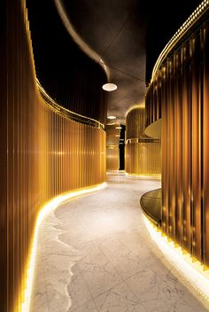 a long hallway with gold walls and lights on either side, leading to an elevator