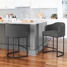 two gray chairs sitting on top of a wooden floor next to an island in a kitchen