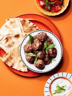 two plates with meatballs and pita bread on an orange tablecloth next to a bowl of yogurt