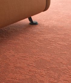 an orange carpet with a brown couch in the background and blue feet resting on it