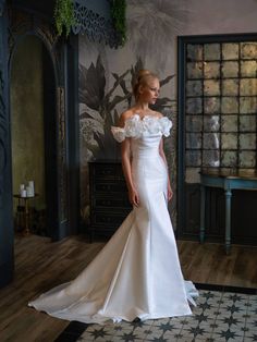 a woman in a white wedding dress standing on a wooden floor next to a wall