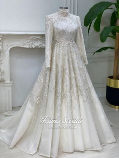 a white wedding gown with long sleeves and beading on the skirt is displayed in front of a fireplace