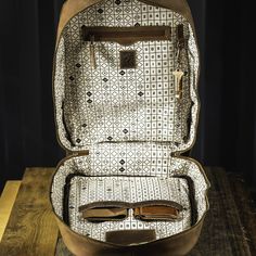 an open suitcase sitting on top of a wooden table next to a pair of glasses