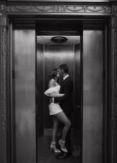 a man and woman kissing while standing in front of an open elevator door with their arms around each other