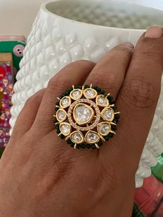 a woman's hand holding a gold ring with white and green stones on it