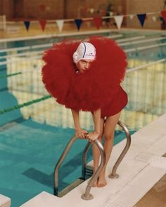 a woman in a red dress and hat leaning on a metal hand rail next to a swimming pool