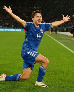 a male soccer player is running on the field with his arms out and hands in the air