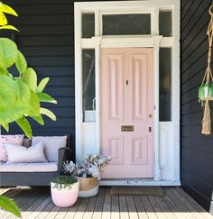 a pink door on a black house with potted plants