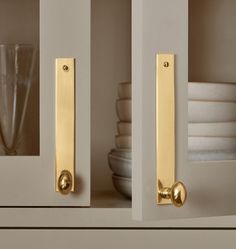 two brass handles on the back of a white cabinet with plates and glasses in it