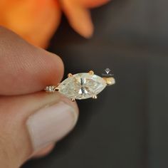 a person is holding an engagement ring with a pear shaped diamond on it's side