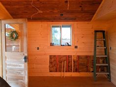 the inside of a house being built with wooden walls and windows, ladders to the door