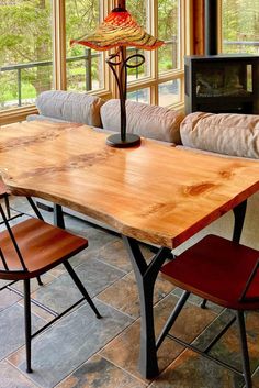 a wooden table with chairs around it in front of a fire place and large windows