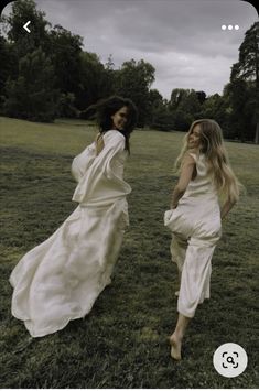 two women in white dresses are walking through the grass