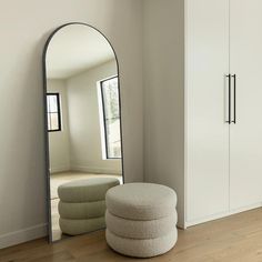 a large mirror sitting on top of a wooden floor next to a white cabinet and ottoman