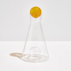 a glass vase with a yellow ball in the bottom and water on the bottom, sitting on a white surface