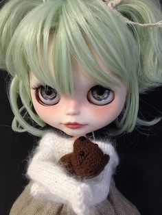 a close up of a doll with green hair wearing a sweater and holding a teddy bear