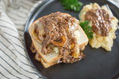 two pieces of bread with meat and gravy on them sitting on a black plate