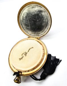 an open compact mirror sitting on top of a white table next to a tassell