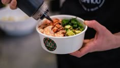 a person is pouring sauce on a bowl of food with shrimp and cucumbers