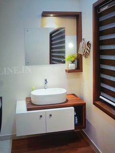 a bathroom sink sitting under a mirror next to a wooden counter top with a vase on it