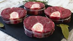 four pieces of raw meat sitting on top of a black plate next to green leaves