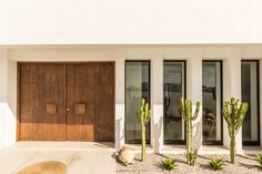 a house with two large wooden doors and cactus plants in front of the entrance to it