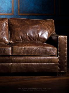 a brown leather couch sitting on top of a wooden floor next to a blue wall