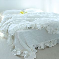 an unmade bed with white sheets and ruffles on the bottom, next to a yellow flower