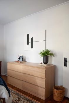 a bed room with a neatly made bed and a wooden dresser next to a plant