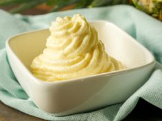 a white bowl filled with whipped cream on top of a blue cloth next to a pineapple