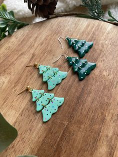 three christmas tree shaped earrings sitting on top of a wooden table