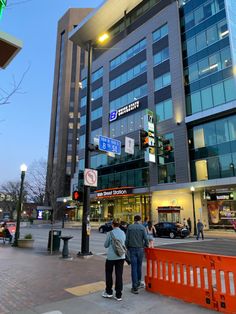 two people are standing on the sidewalk in front of a tall building with many windows