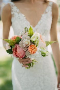 a woman in a wedding dress holding a bridal bouquet with flowers and greenery