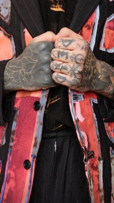 a man with tattoos on his arm and hand in front of him, wearing a colorful jacket