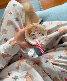 a person in pajamas holding a drink with sprinkles and candy on it