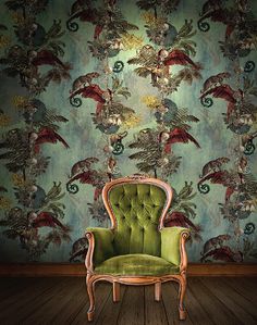 a green chair sitting on top of a wooden floor next to a wall covered in birds