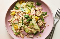 a pink plate topped with salad next to a fork and knife on a white table