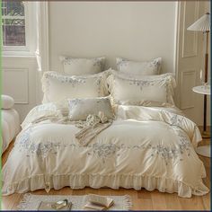 a bed with white comforters and pillows in a room next to a lamp on the floor