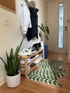 a coat rack with shoes and other items on it next to a plant in a room