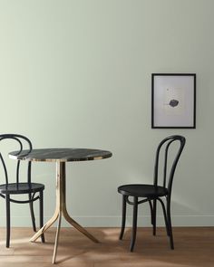 two chairs and a table in front of a white wall with a black framed picture on it