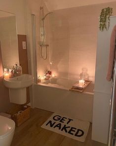 a bathroom with candles on the floor and a bathtub next to it, along with a rug that says get naked