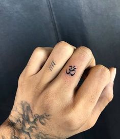 a person's hand with a small tattoo on their left wrist and an om symbol tattooed on the middle finger