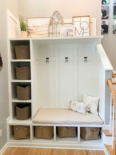 a white bench with baskets underneath it and some pictures hanging on the wall behind it