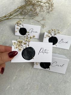 three black and white place cards with flowers in the middle, one being held by a woman's hand