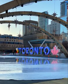 the toronto sign is lit up in front of some tall buildings and ice skating rinks