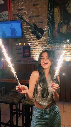 a woman holding two sparklers in her hands while standing next to a table with a guitar on it