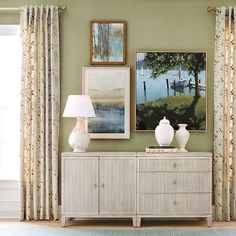 a living room with green walls and pictures on the wall, two vases sitting on top of a dresser