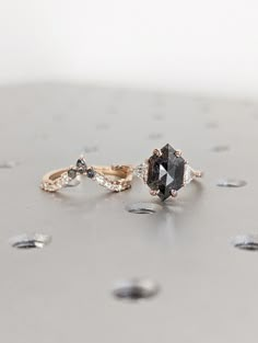 two engagement rings sitting on top of each other with different colored stones around them and one has a black diamond in the middle